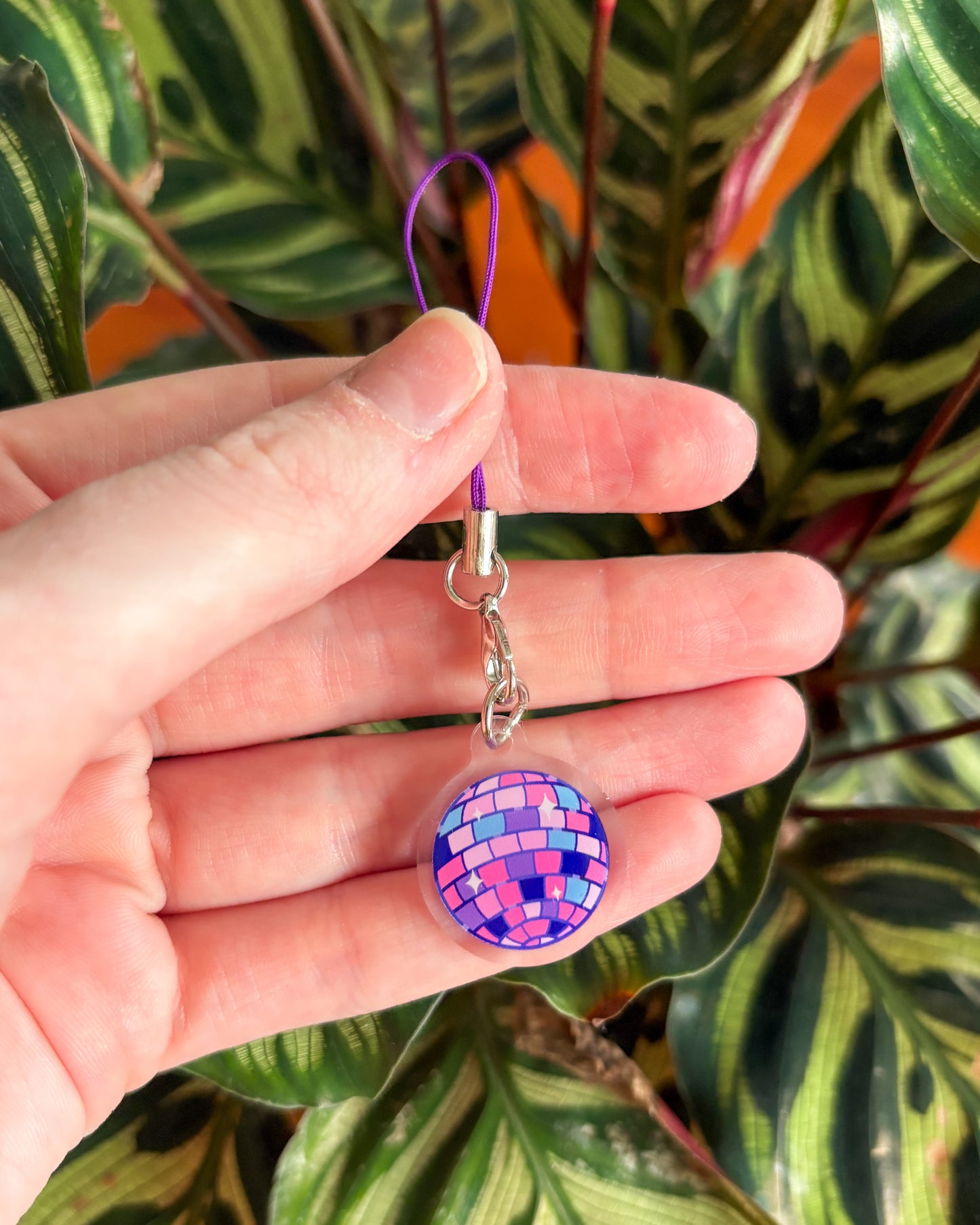 Hand holding a colorful keychain with a DISCO BALL design against a leafy background