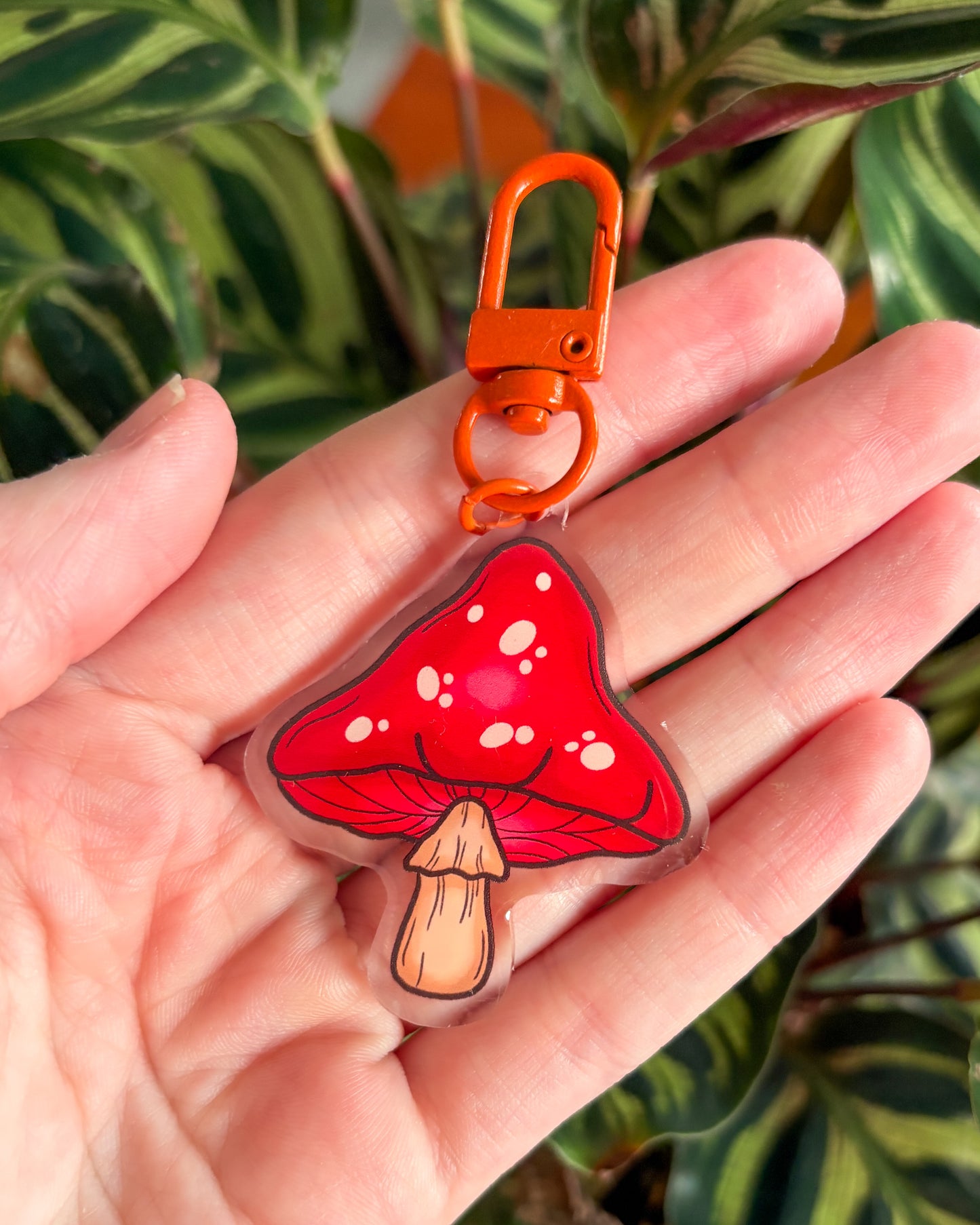 Red mushroom-shaped keychain with an orange clip held in a hand against a plant background