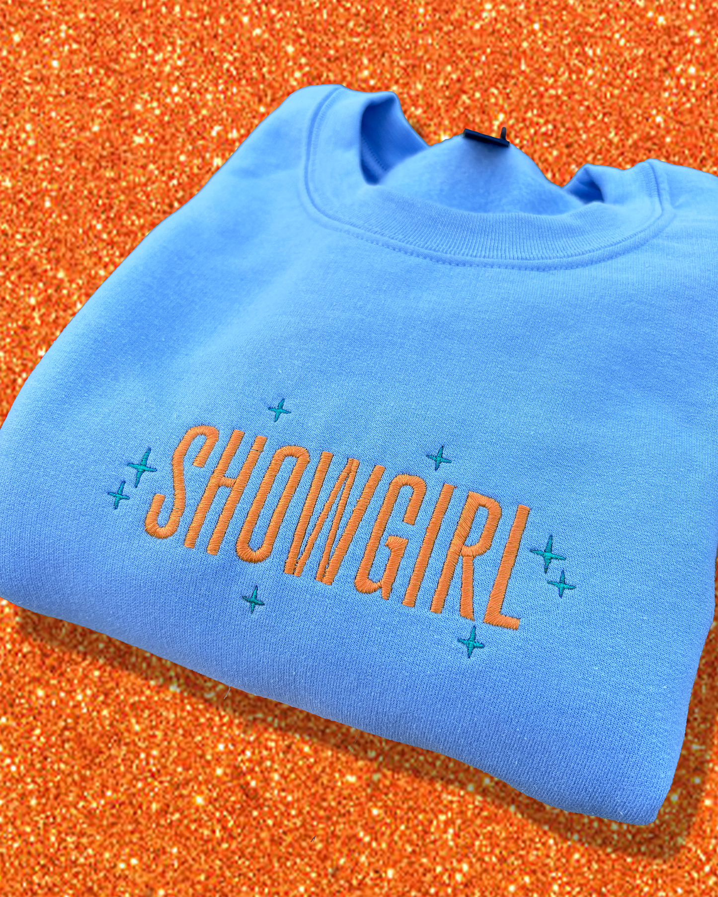 Blue sweatshirt with 'SHOWGIRL' text on an orange glittery background