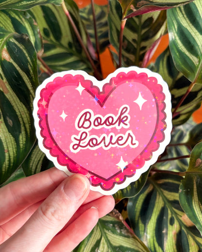 Heart-shaped 'Book Lover' sticker held in front of leafy green plants