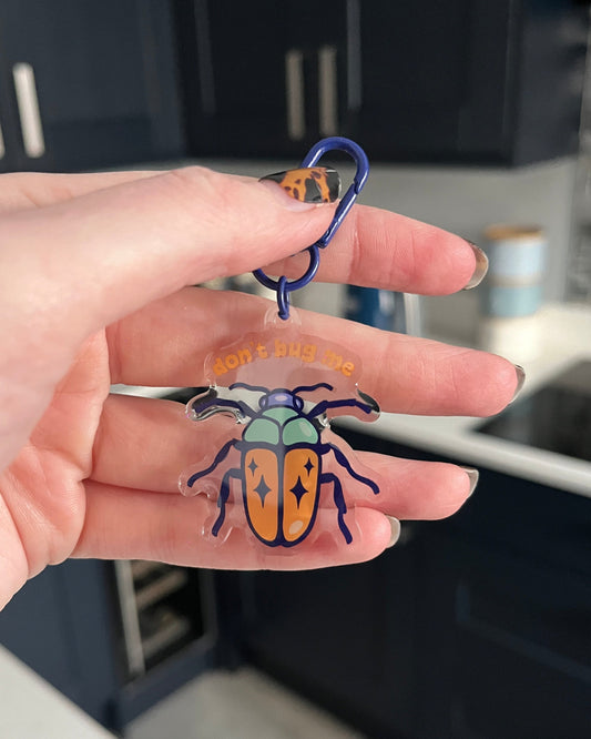 A hand holding a blue beetle-shaped keyring with a swivel clasp.
