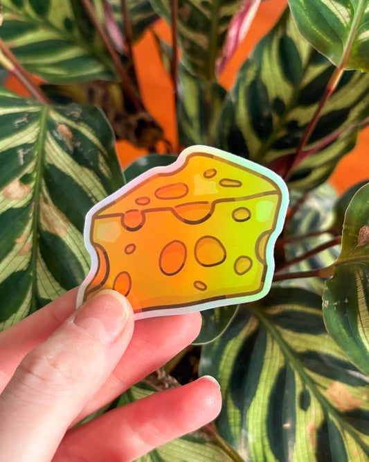 Hand holding a colorful cheese slice sticker in front of leafy plants