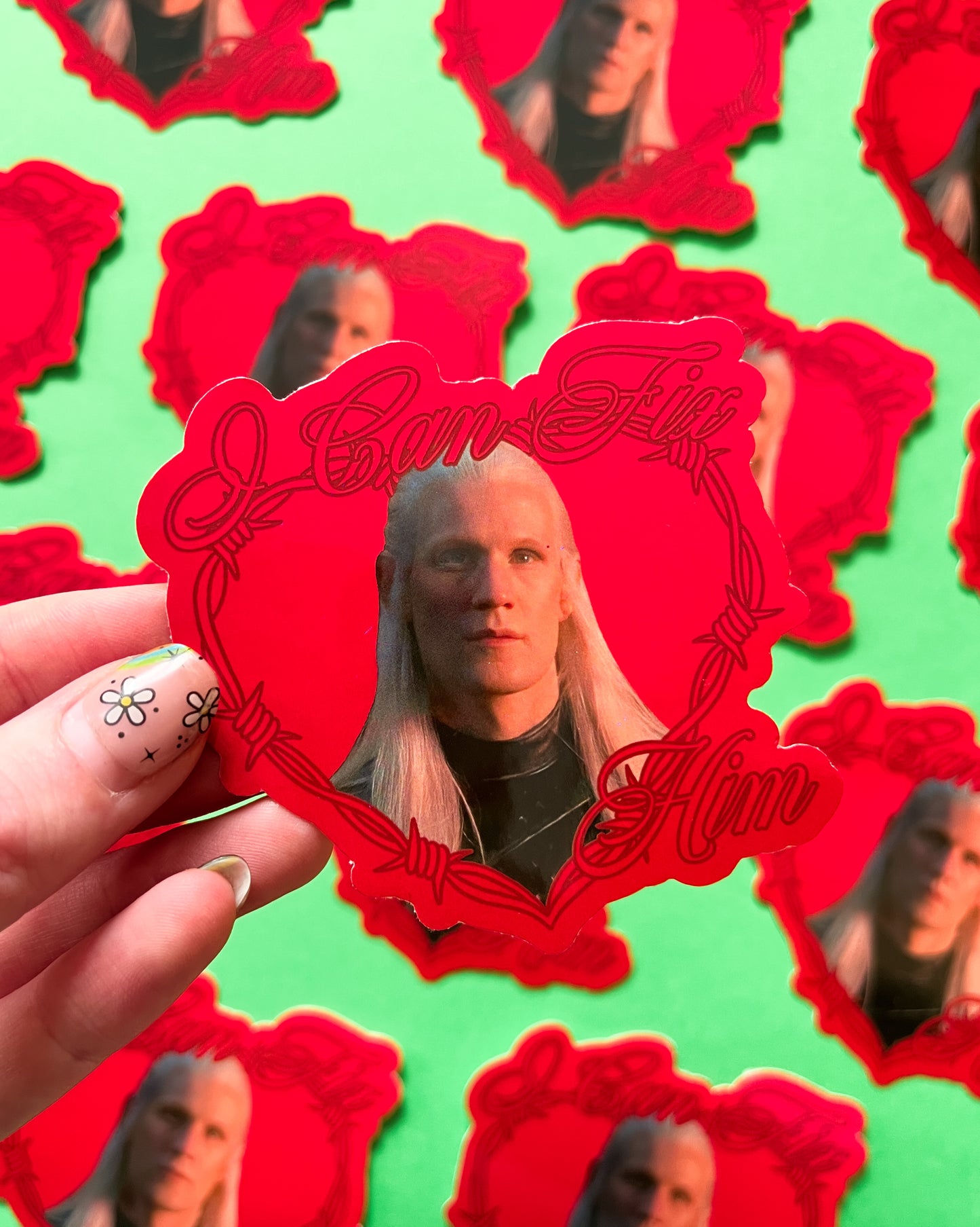 A person holding a vinyl sticker with an image of Daemon Targaryen, and other similar stickers visible in the background.