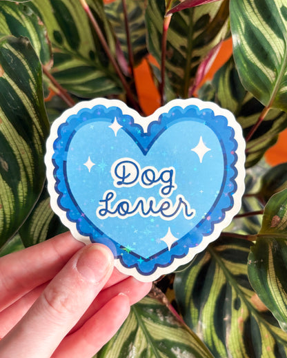 Heart-shaped sticker with 'Dog Lover' text held in front of leafy plants