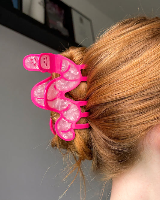 Person with pink worm hair clip in their hair against a neutral background
