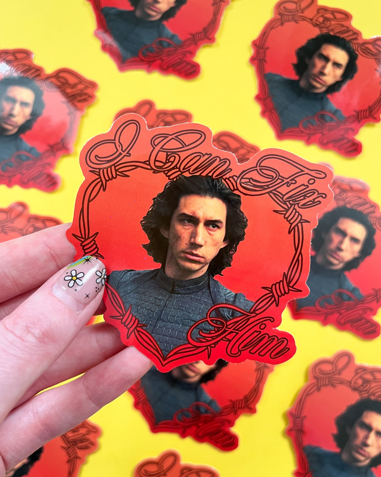 A person holding a vinyl sticker of Kylo Ren with the text 'I Can Fix Him' on a yellow background, where other similar stickers are also visible.