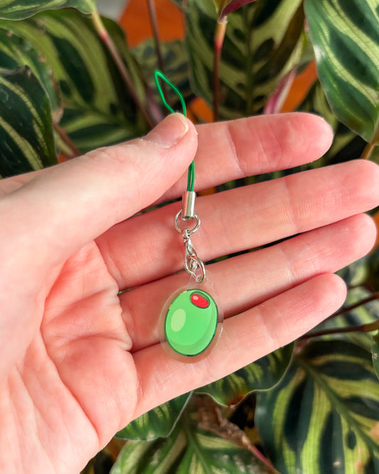 Hand holding an olive phone charm against a leafy background