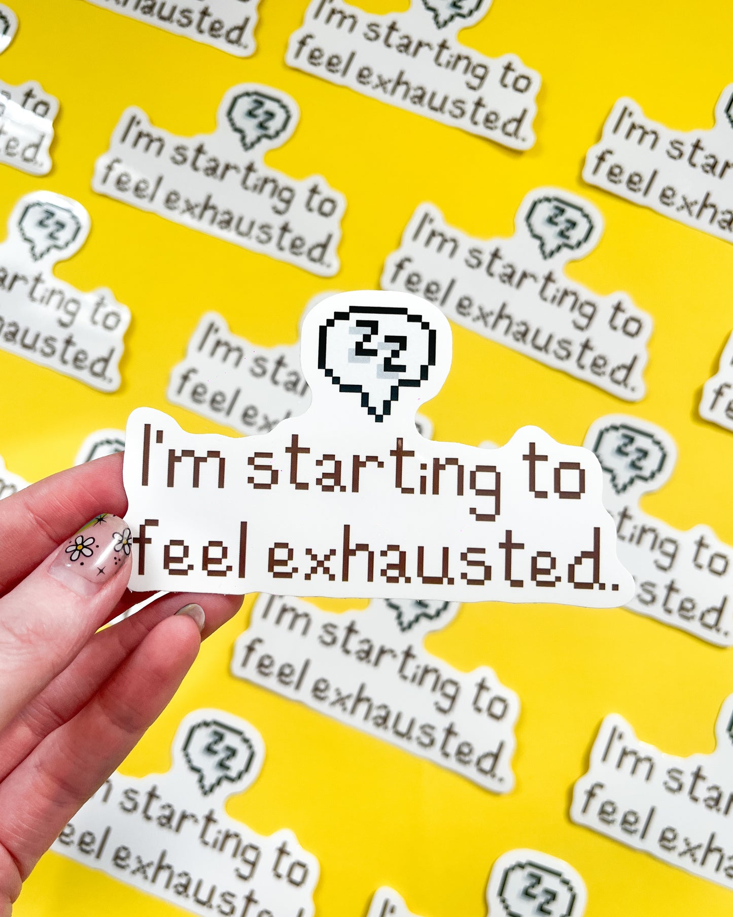 A vinyl sticker with the phrase 'I'm starting to feel exhausted.' printed in a white and grey color scheme, held against a background of the same sticker repeated.