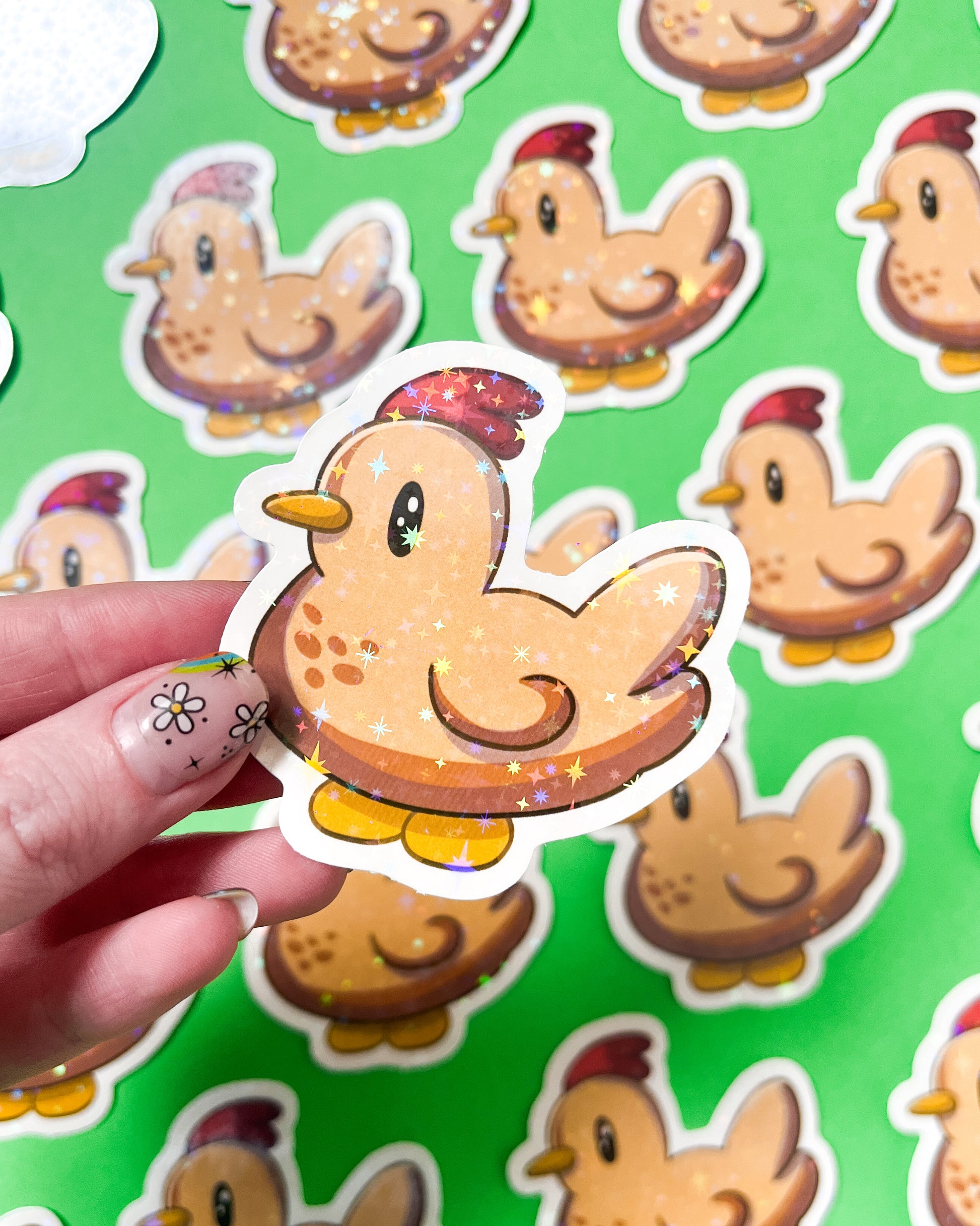 A person holding a vinyl sticker of a chicken with a holographic background, featuring multiple chicken stickers in the background.