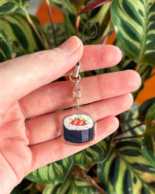 Hand holding a keychain shaped like a piece of sushi with a plant in the background