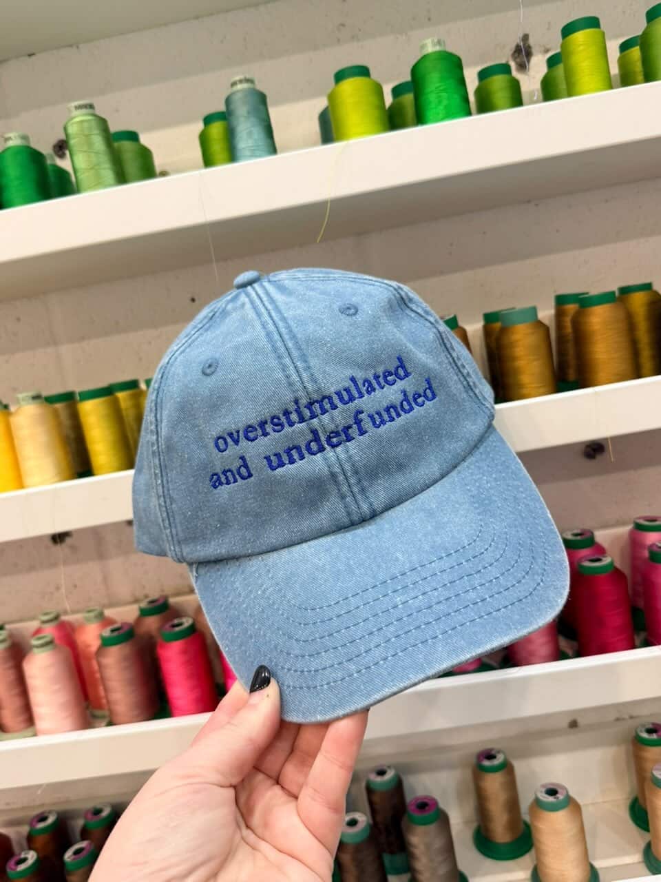 Blue cap with text held in front of spools of thread