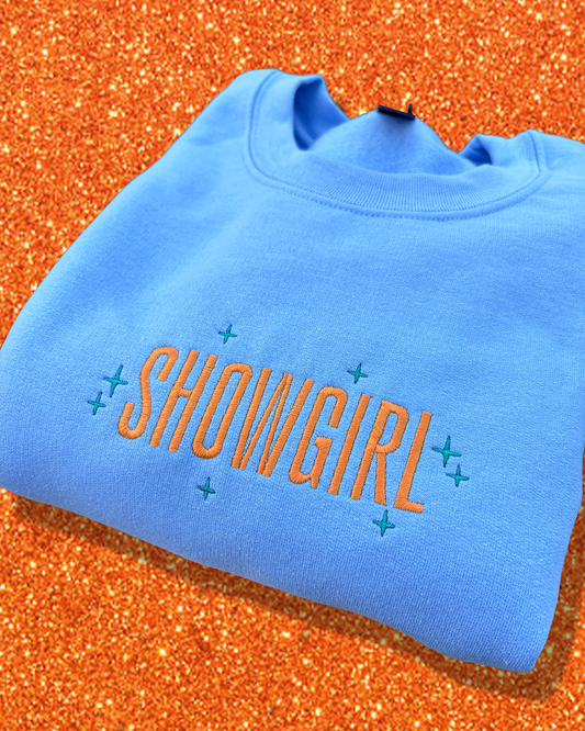 Blue sweatshirt with 'SHOWGIRL' text on an orange glittery background